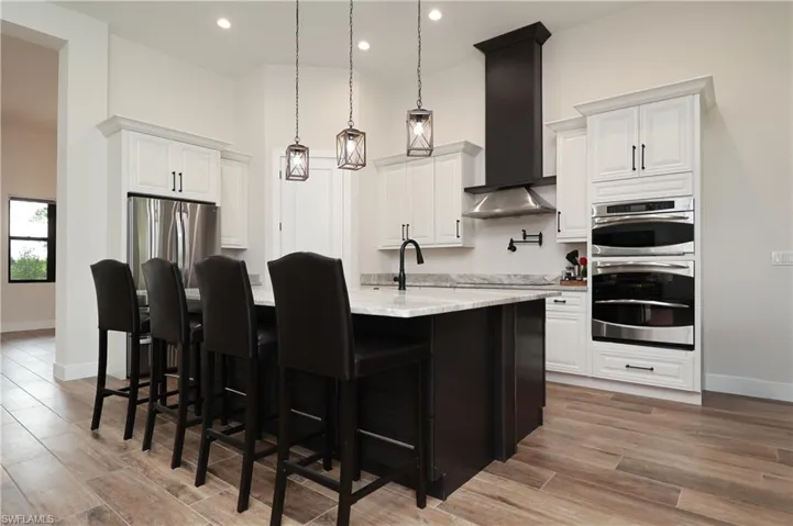 Kitchen featuring a high ceiling, decorative light fixtures, light wood-style flooring, two tone cabinets, and stainless steel appliances