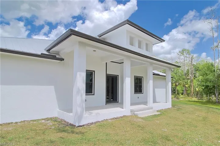 Back of property featuring covered porch, a yard, stucco siding, and a metal roof