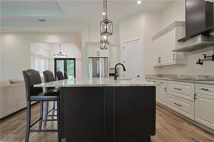 Kitchen featuring decorative light fixtures, an island with sink, a breakfast bar area, light stone countertops, and two tone cabinets