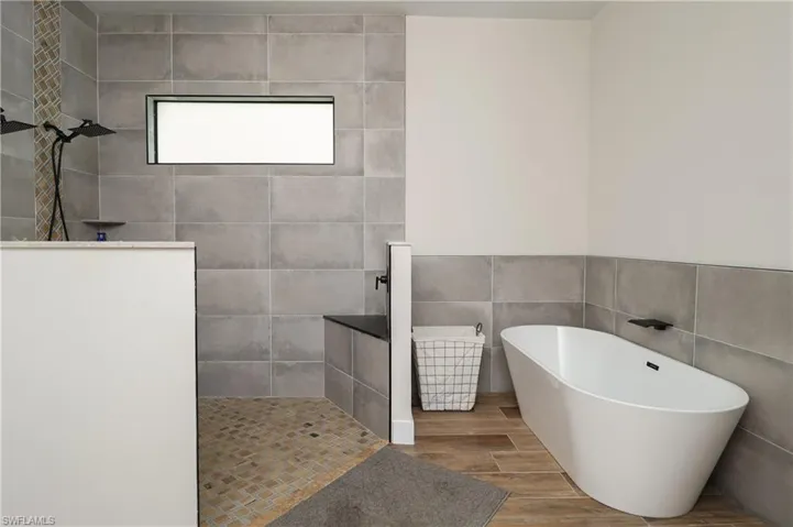 Bathroom featuring a freestanding bath, tile walls, a walk in shower, wood tiled floors, and pet washing area