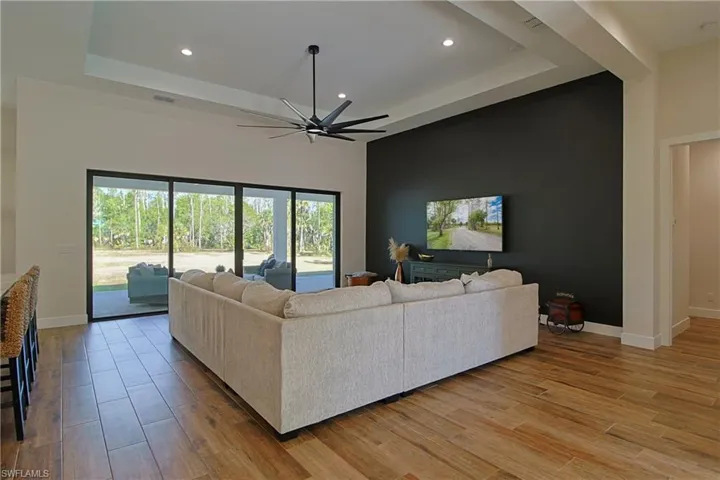 Living room with a raised ceiling, ceiling fan, light wood-type flooring, and recessed lighting