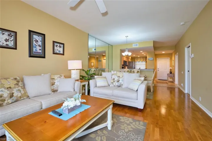 Living area featuring ceiling fan with notable chandelier, visible vents, wood finished floors, and baseboards