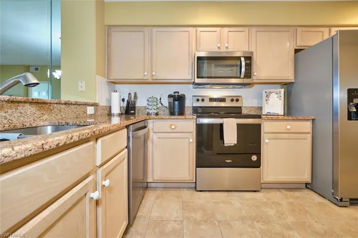 Kitchen with light brown cabinetry, a sink, light tile patterned flooring, light stone counters, and appliances with stainless steel finishes