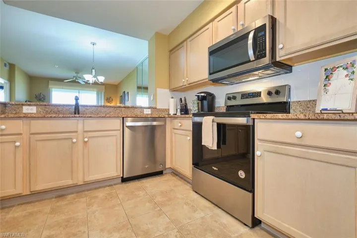Kitchen with stainless steel appliances, tasteful backsplash, light stone counters, an inviting chandelier, and light brown cabinetry