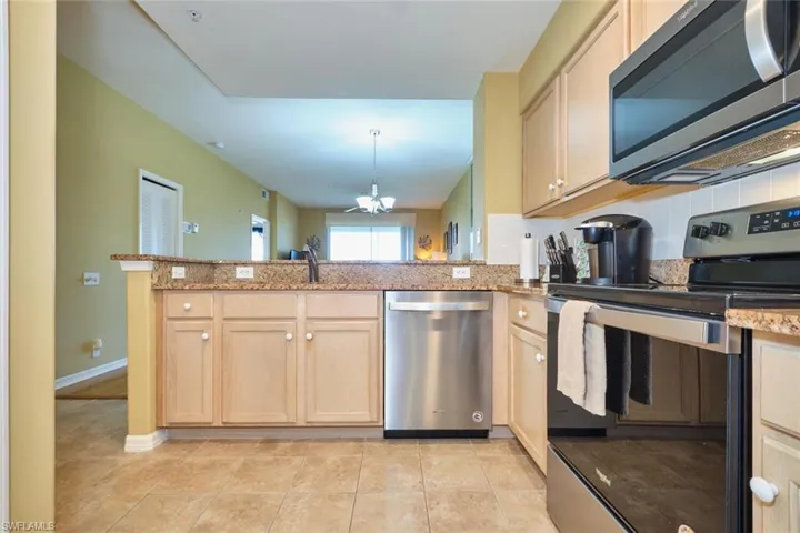 Kitchen with a peninsula, stainless steel appliances, light brown cabinets, a sink, and light stone counters