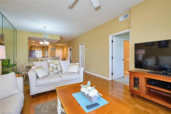 Living room with ceiling fan with notable chandelier, visible vents, wood finished floors, and baseboards