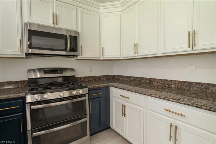 Kitchen featuring stainless steel appliances, white cabinetry, and dark stone countertops