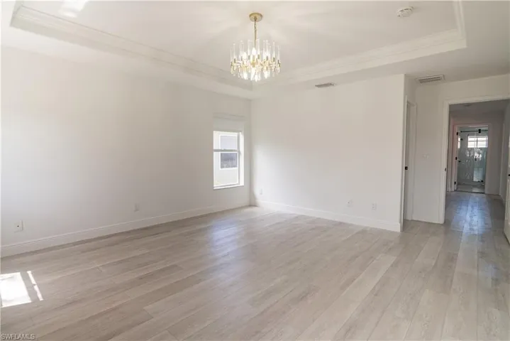 Unfurnished room with a raised ceiling, hanging lights, crown molding, and light wood-style floors