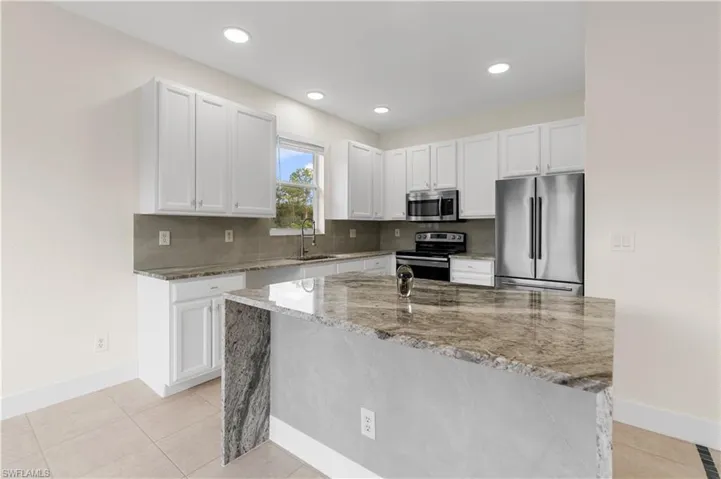 Kitchen featuring appliances with stainless steel finishes, baseboards, light stone countertops, and white cabinetry