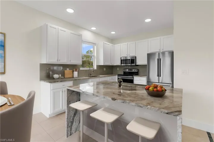 Kitchen with a kitchen breakfast bar, white cabinets, and stainless steel appliances
