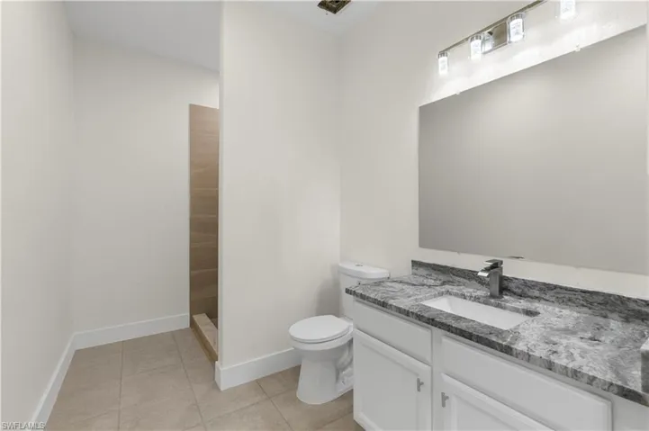 Bathroom with tile patterned flooring, a tile shower, vanity, baseboards, and toilet