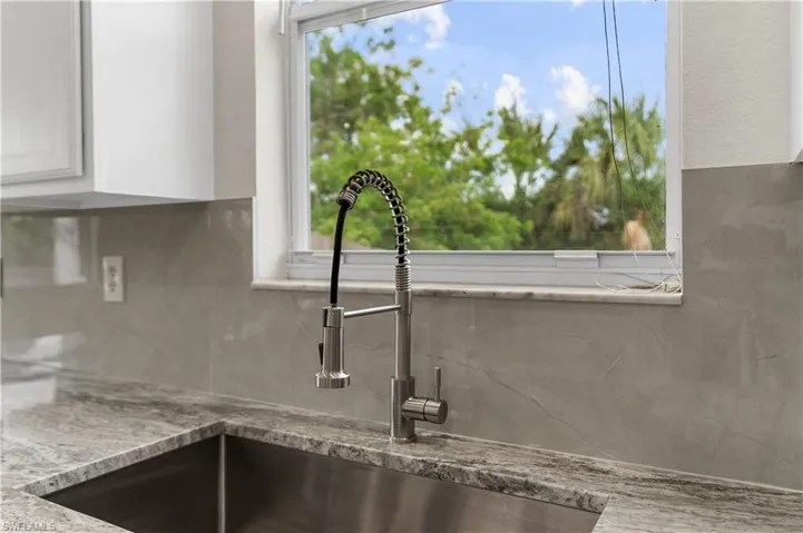 Details with a sink, white cabinets, light stone countertops, and backsplash