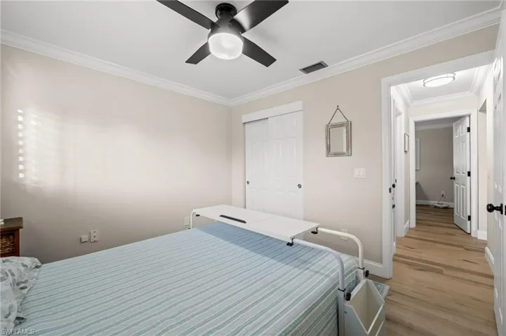 Neutral-toned interior featuring wood-finish flooring, crown molding, a central ceiling fan with integrated lighting, and white six-panel closet doors