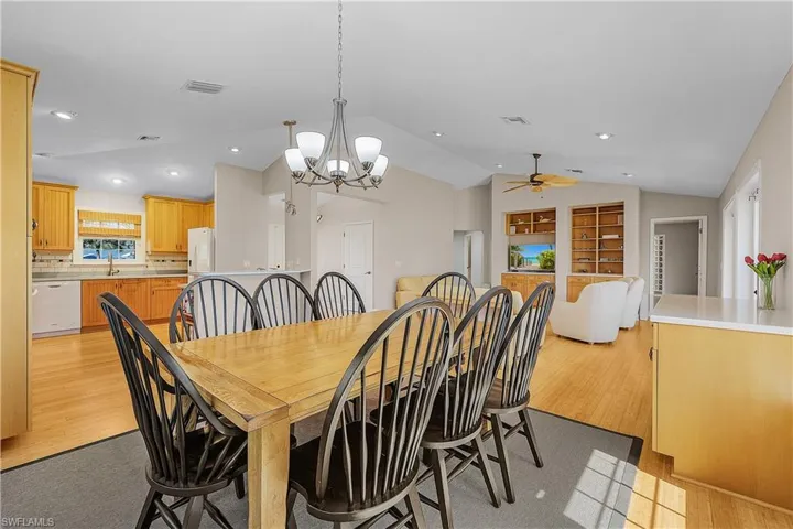 Dining room with lofted ceiling, sink, ceiling fan with notable chandelier, and light wood-type flooring