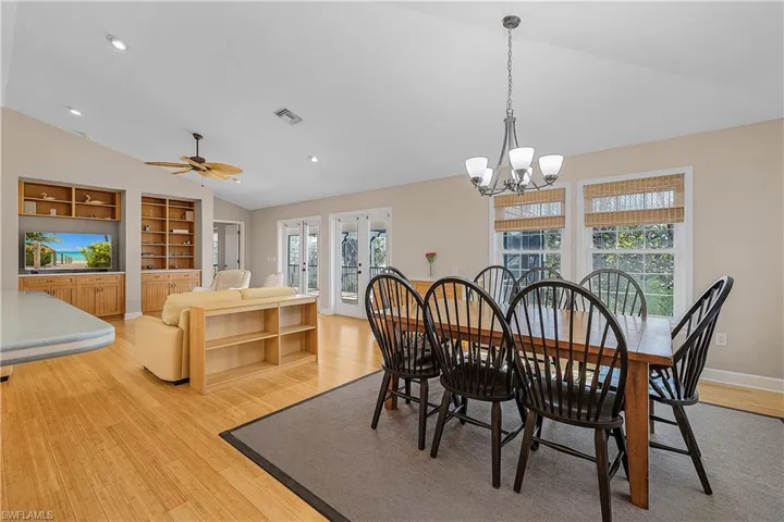 Dining area featuring lofted ceiling, built in features, light hardwood / wood-style floors, ceiling fan with notable chandelier, and french doors