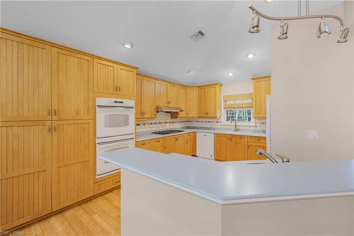 Kitchen with backsplash, sink, white appliances, and wood-style flooring