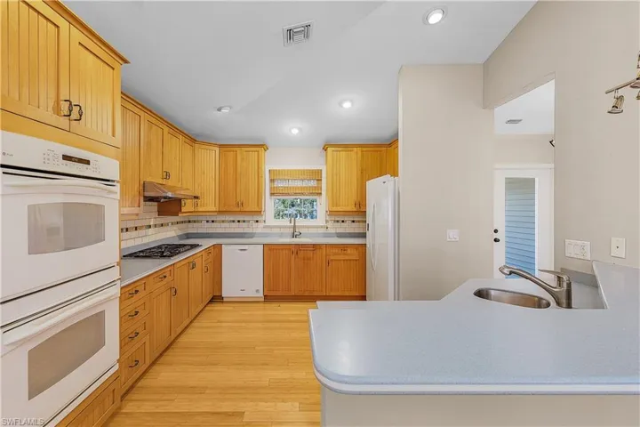 Kitchen with sink, white appliances, wood-style floors, and backsplash