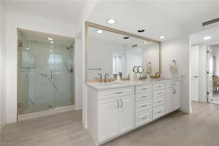 Bathroom with double vanity, a marble finish shower, light wood-type flooring, and recessed lighting