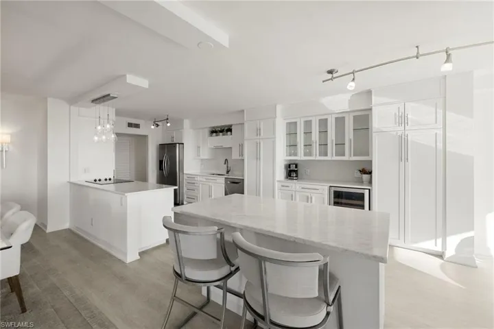 Kitchen with a breakfast bar, white cabinets, light wood-type flooring, beverage cooler, and track lighting