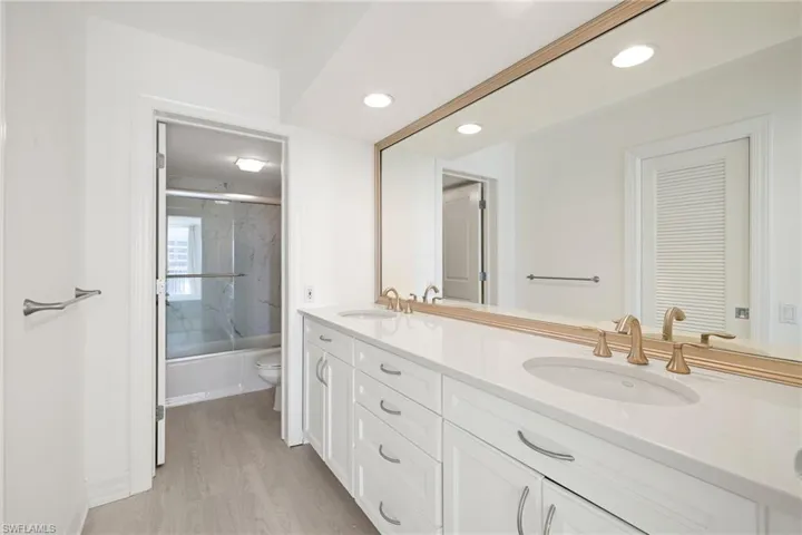 Full bathroom featuring enclosed tub / shower combo, double vanity, light wood-style flooring, and recessed lighting