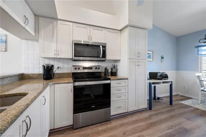 Kitchen with appliances with stainless steel finishes, tasteful backsplash, light stone countertops, light hardwood / wood-style floors, and white cabinets