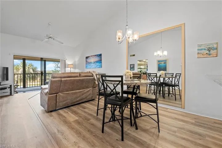 Dining area with ceiling fan with notable chandelier, high vaulted ceiling, and light hardwood / wood-style flooring