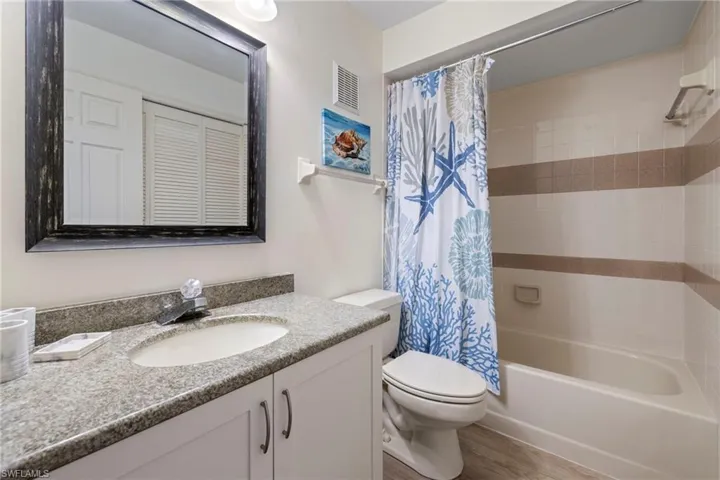 Full bathroom with hardwood / wood-style flooring, vanity, toilet, and shower / bath combo with shower curtain