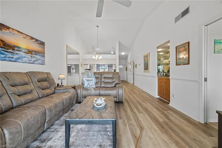 Living room featuring high vaulted ceiling, ceiling fan with notable chandelier, and light wood-type flooring