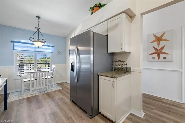 Kitchen with light hardwood / wood-style flooring, stainless steel fridge, hanging light fixtures, and white cabinets