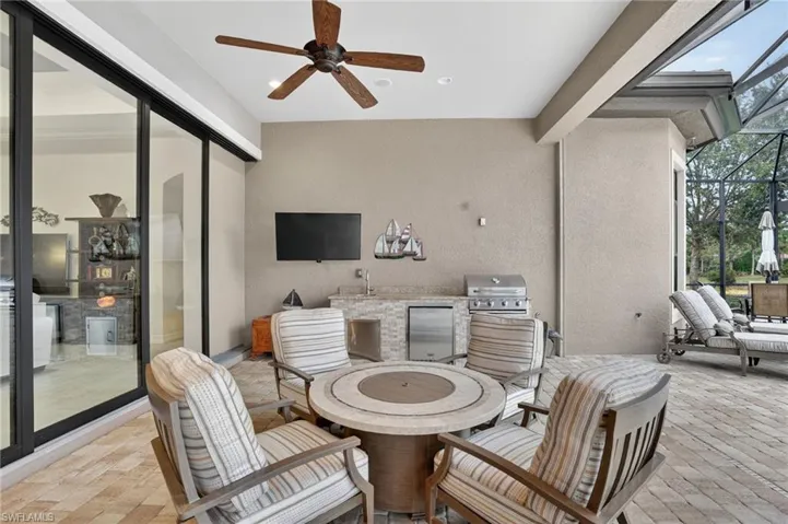 View of lanai with gas fire pit, four chairs, new TV. outdoor kitchen with new refrigerator and new gas grill, Storm Smart motorized hurricane proof  screens on all lanai openings.
