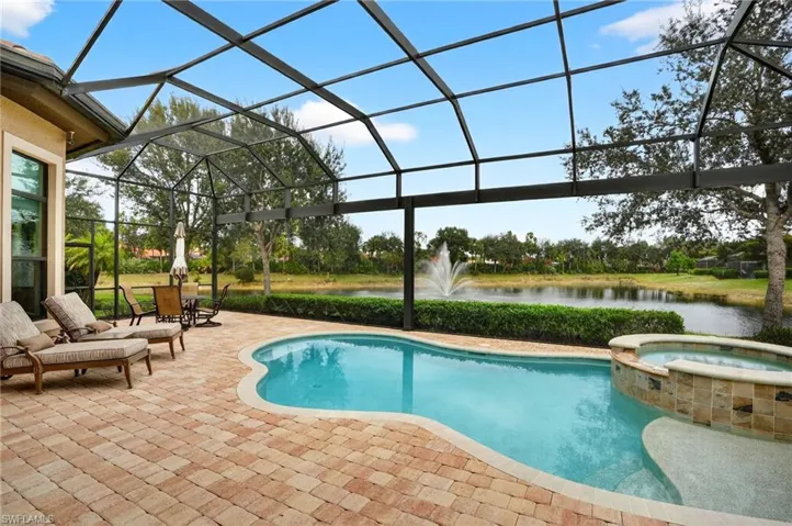 View of  pool featuring the lanai deck, panoramic pool cage screen, spa, and wide water lake views.