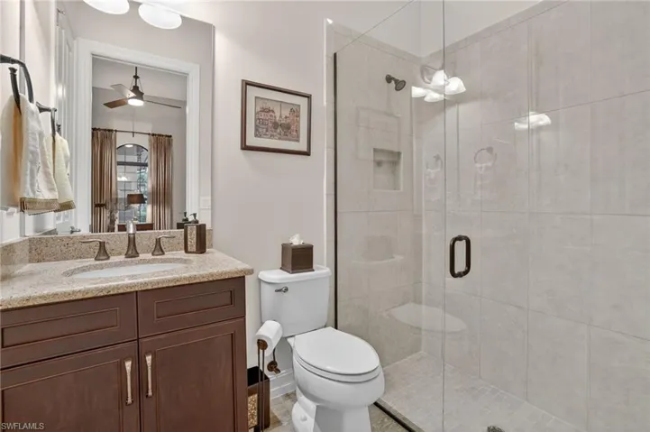 Full bathroom in den/flex room featuring vanity, frameless glass shower door, granite counter,and porcelain tiled shower walls, and porcelain wood like plank floor.