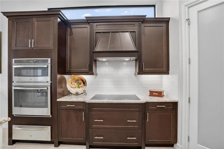 featuring upgraded wood cabinetry, custom range hood, stainless steel double oven, backsplash, and a warming drawer