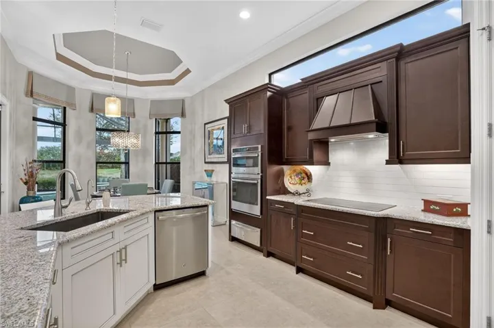 Featuring crown molding, tray ceiling, hanging light fixtures, stainless steel appliances, light stone counters, and morning breakfast room