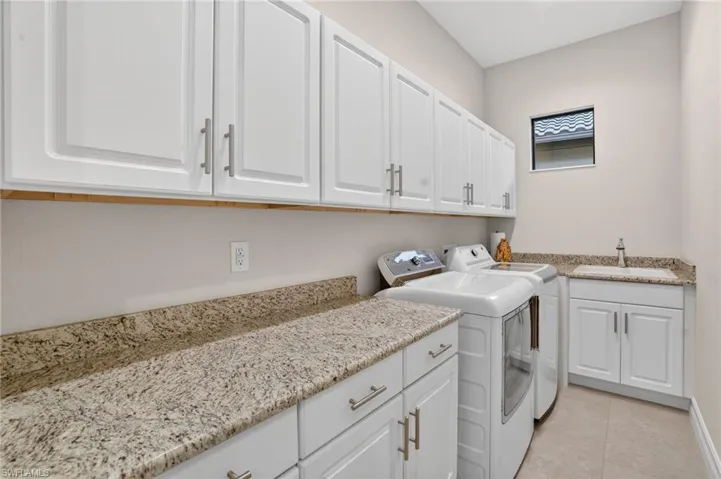 Spacious laundry room featuring LG washer and dryer, laundry tub with vanity, and a window with impact hurricane glass