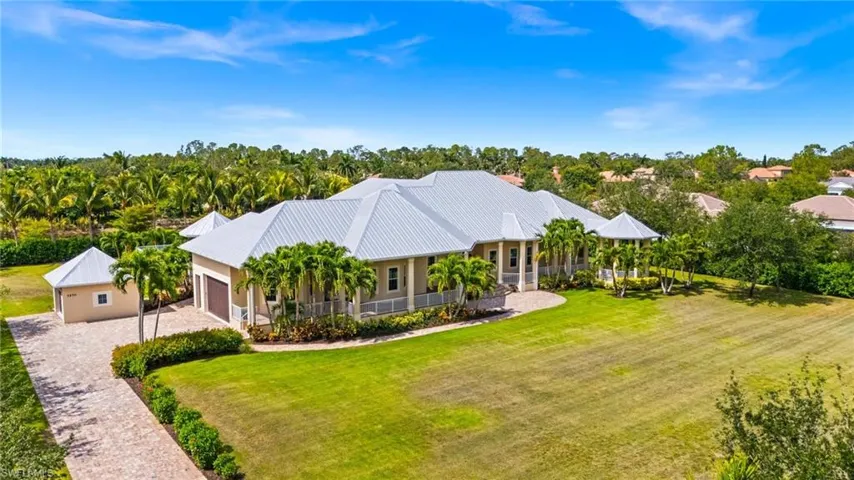 View of front of home featuring an attached garage, driveway, covered porch, a front yard, and metal roof