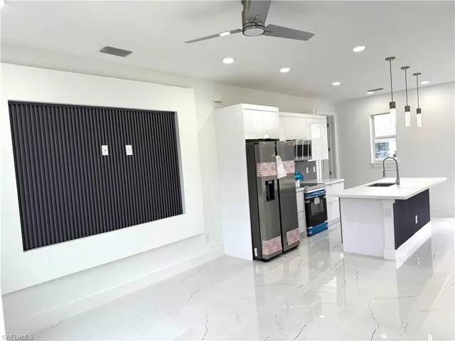 Kitchen with appliances with stainless steel finishes, light marble finish floors, recessed lighting, pendant lighting, and white cabinetry