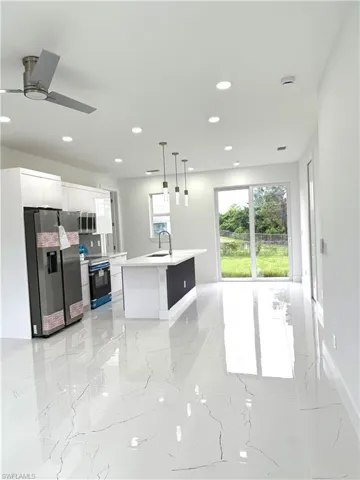 Kitchen with white cabinetry, appliances with stainless steel finishes, light marble finish flooring, hanging light fixtures, and a center island with sink