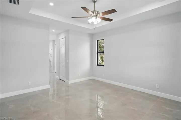 Spare room with a tray ceiling, recessed lighting, a ceiling fan, and light marble finish floors