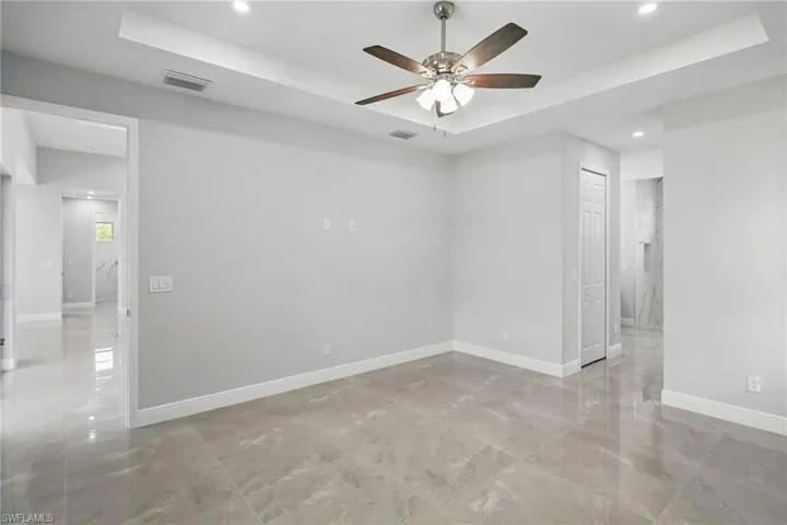Empty room featuring a tray ceiling, recessed lighting, light marble finish floors, and ceiling fan