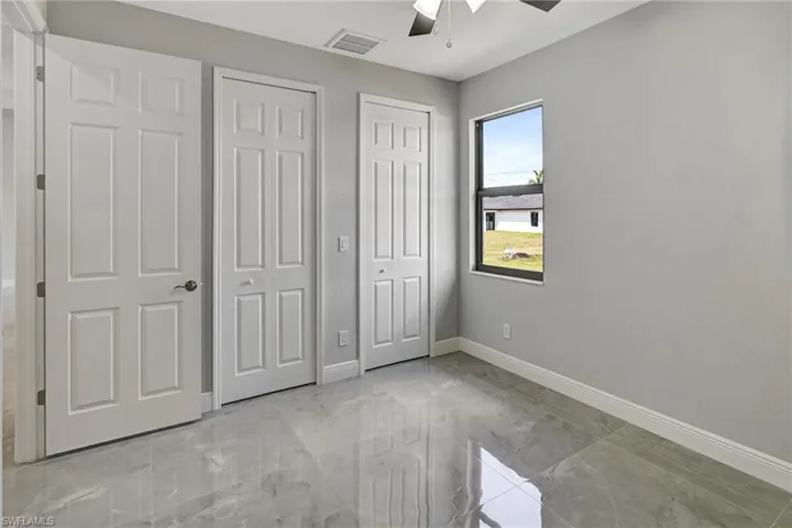 Unfurnished bedroom with two closets, a ceiling fan, and light marble finish flooring