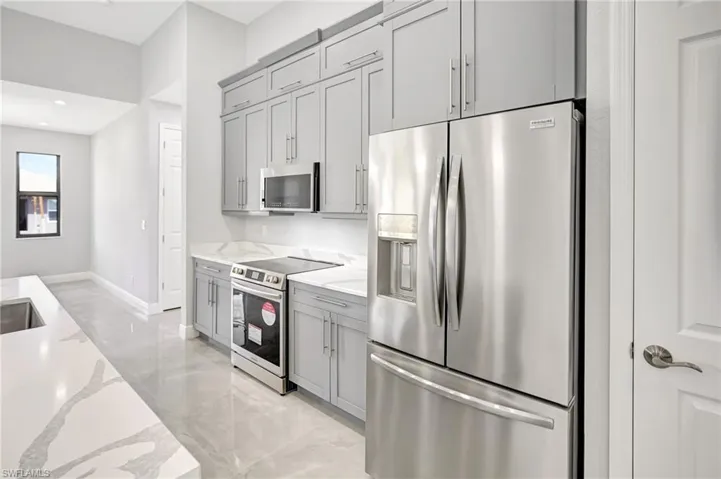 Kitchen with appliances with stainless steel finishes, light stone counters, light marble finish floors, gray cabinetry, and recessed lighting