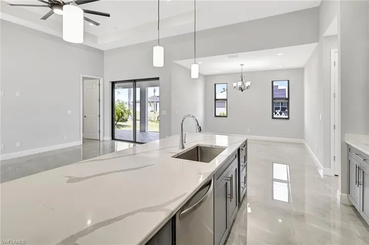 Kitchen with light stone countertops, decorative light fixtures, stainless steel dishwasher, open floor plan, and a chandelier