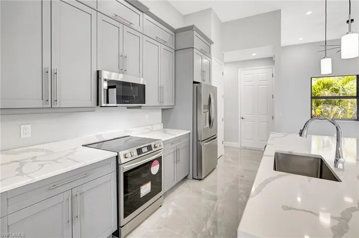 Kitchen featuring appliances with stainless steel finishes, hanging light fixtures, light stone countertops, gray cabinetry, and light marble finish flooring