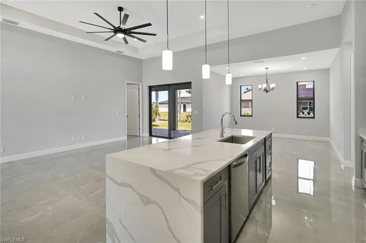 Kitchen featuring hanging light fixtures, light stone counters, open floor plan, stainless steel dishwasher, and a kitchen island with sink