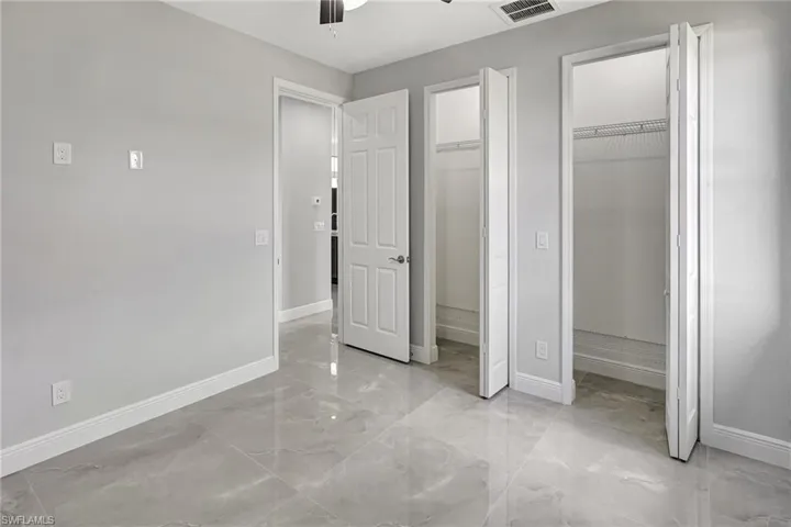 Unfurnished bedroom with multiple closets, ceiling fan, and light marble finish floors