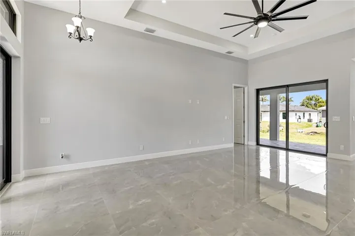 Spare room with a towering ceiling, light marble finish flooring, a tray ceiling, a chandelier, and ceiling fan