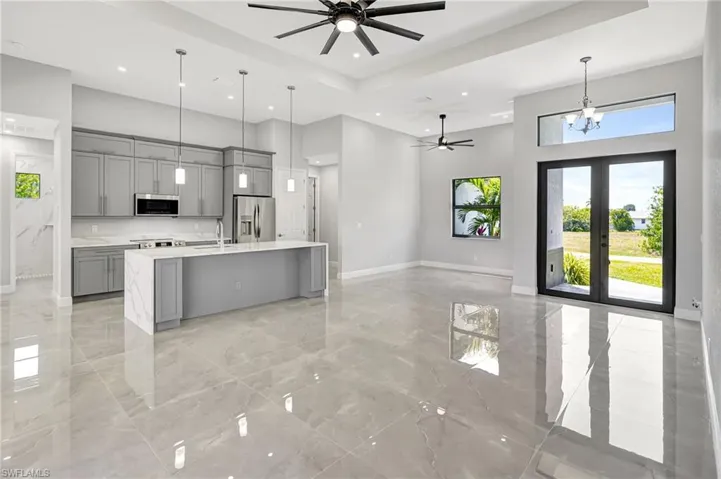 Kitchen featuring gray cabinets, open floor plan, a ceiling fan, a towering ceiling, and a center island with sink