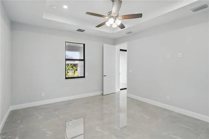 Spare room featuring a tray ceiling, light marble finish floors, and a ceiling fan