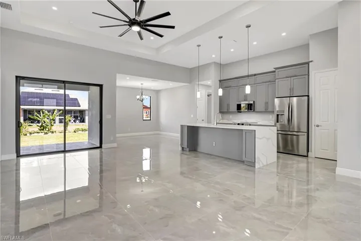 Kitchen with gray cabinets, open floor plan, appliances with stainless steel finishes, a center island with sink, and decorative light fixtures